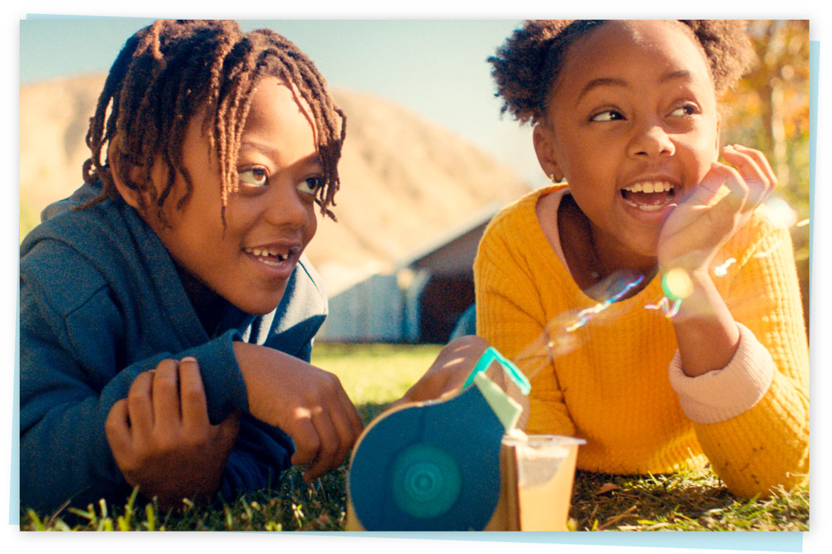 Two children laying on the grass and playing with a monthly science kit