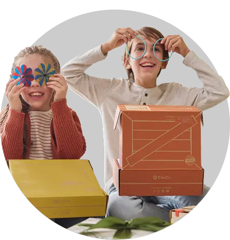 A joyful young boy looks on with an excited expression as he holds an open KiwiCo subscription box filled with activities from the Robots and Coding project.